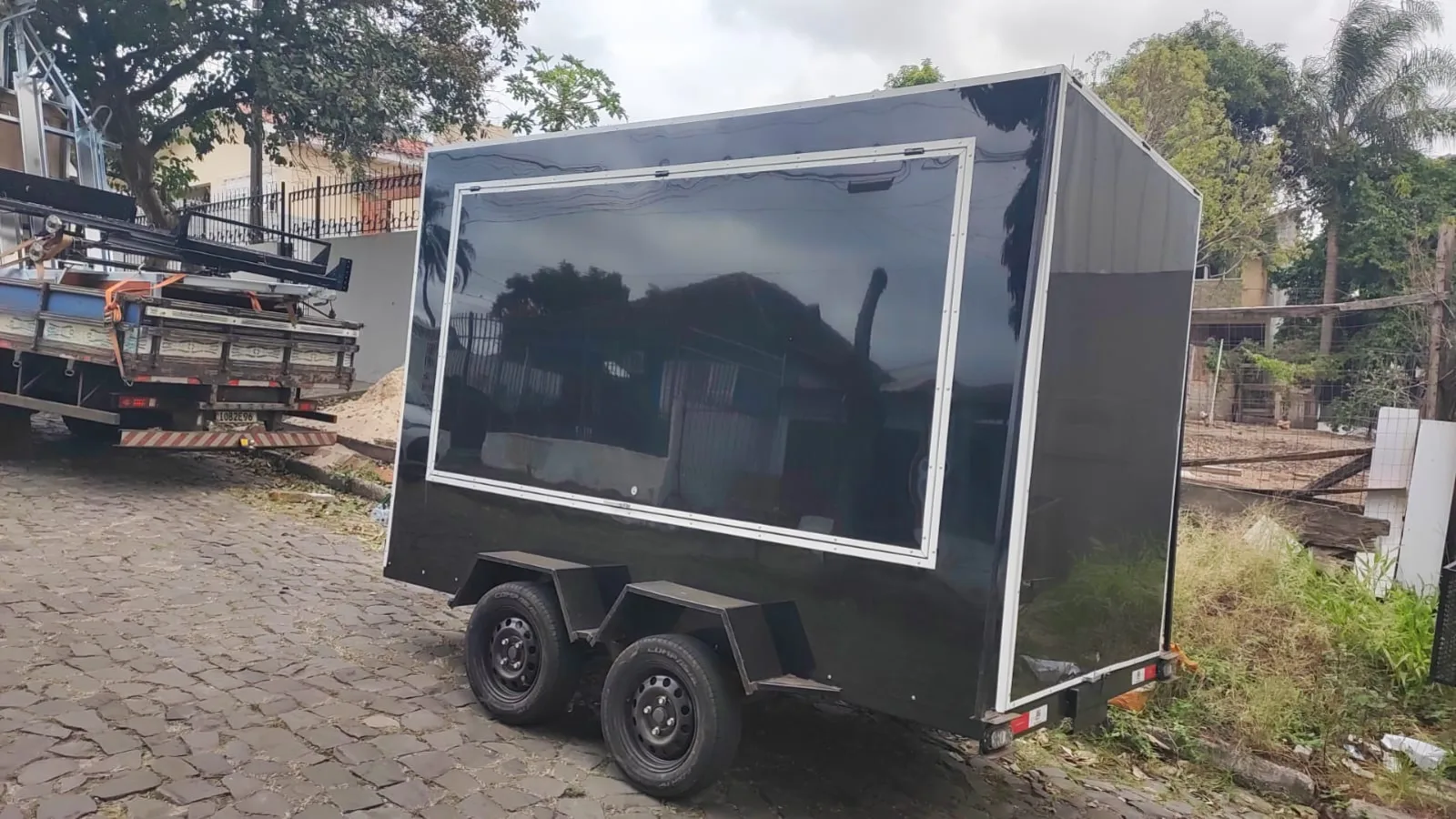 Reboque fechado de dois eixos com vidro na lateral, vista de frente