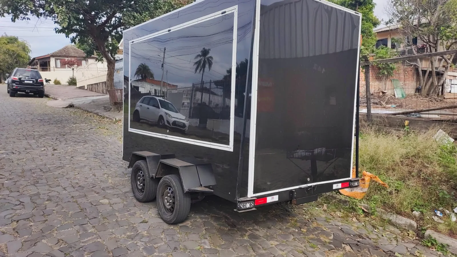 Reboque fechado de dois eixos com laterais escuras, estacionado na rua