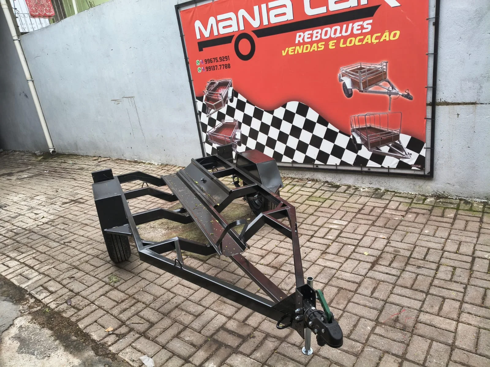 Reboque preto para moto visto de frente, com engate e suporte de roda
