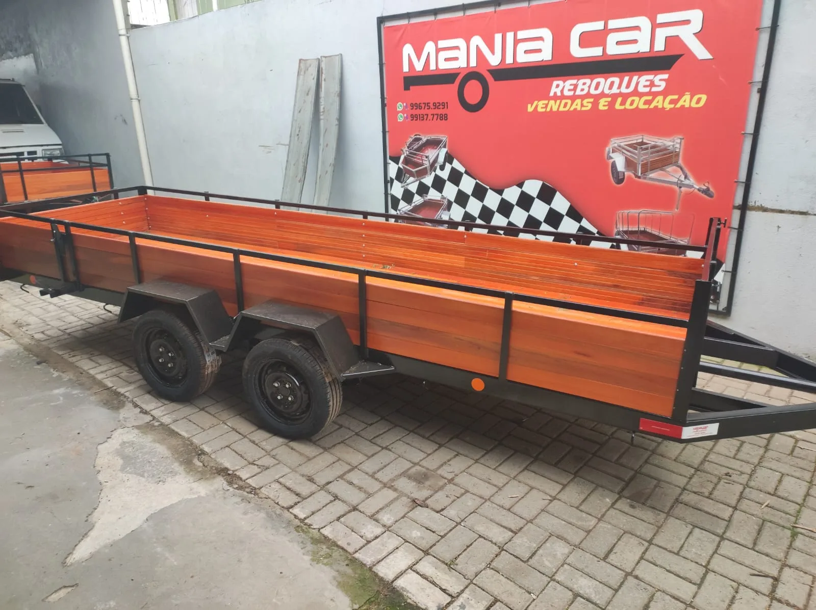Reboque longo de dois eixos com laterais de madeira ao lado do painel da Mania Car