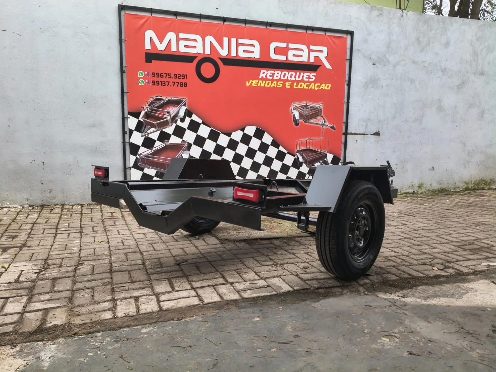 Reboque preto para moto com engate e para-lamas, no pátio da loja
